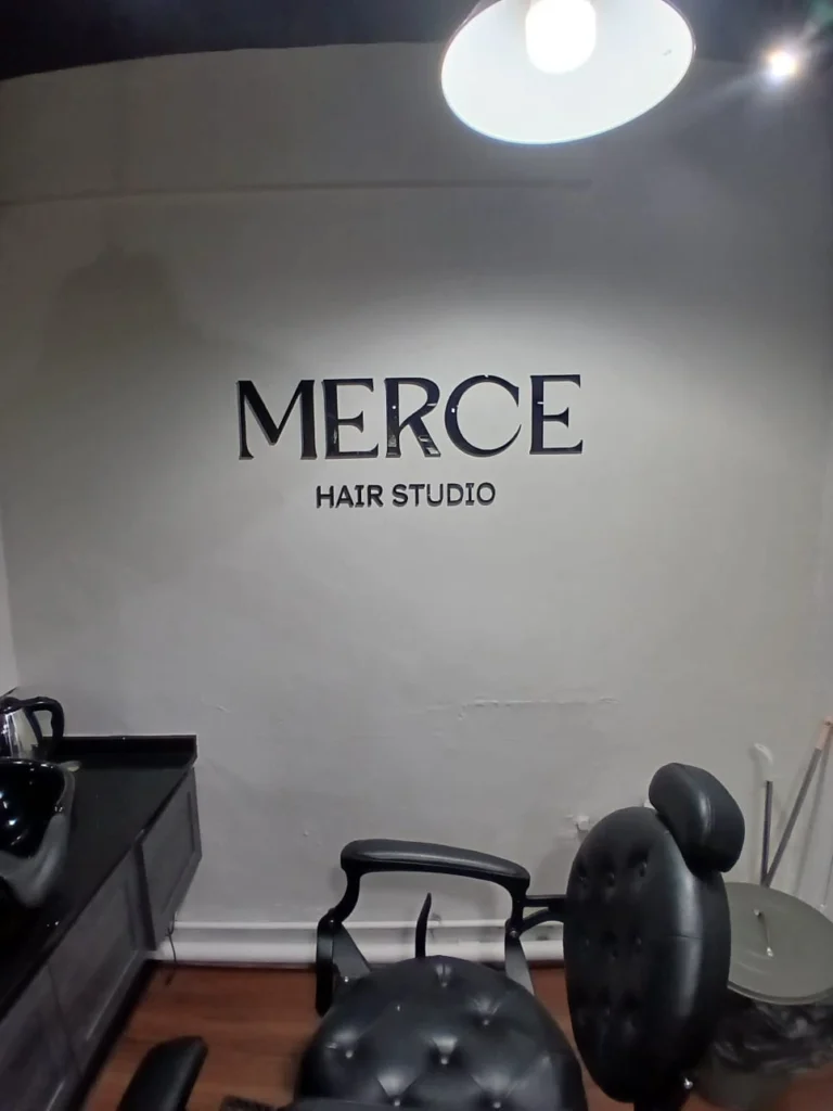 Sleek black 3D acrylic wall lettering reading "MERCE HAIR STUDIO" mounted inside a modern salon setting