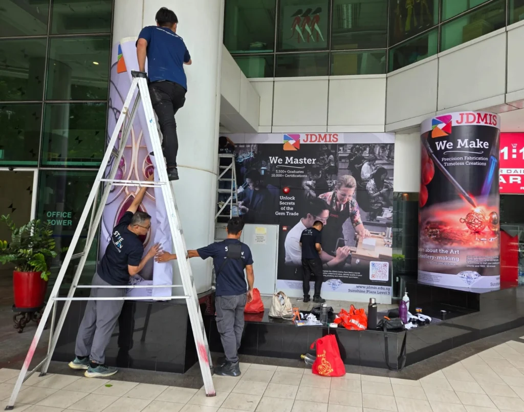 Workers are installing large-format vinyl wall wraps and pillar banners printed with promotional images
