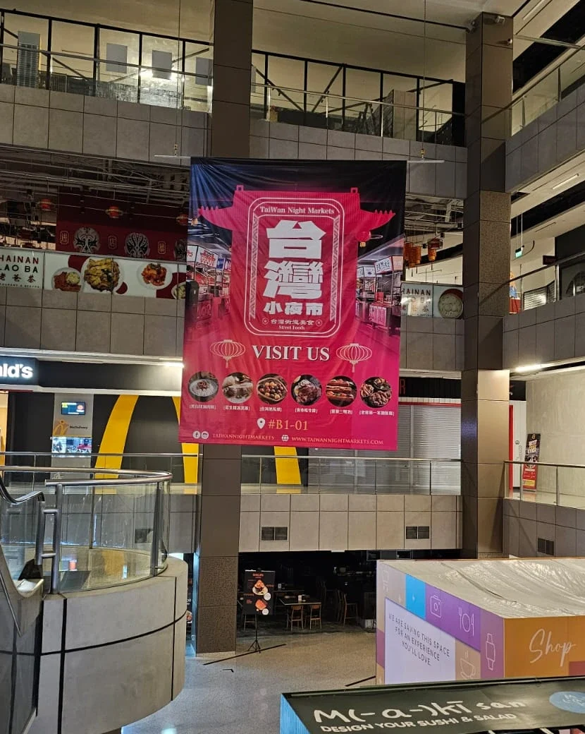A large, vertically hanging red and black promotional banner for "TaiWan Night Markets" features bold Chinese characters and food graphics