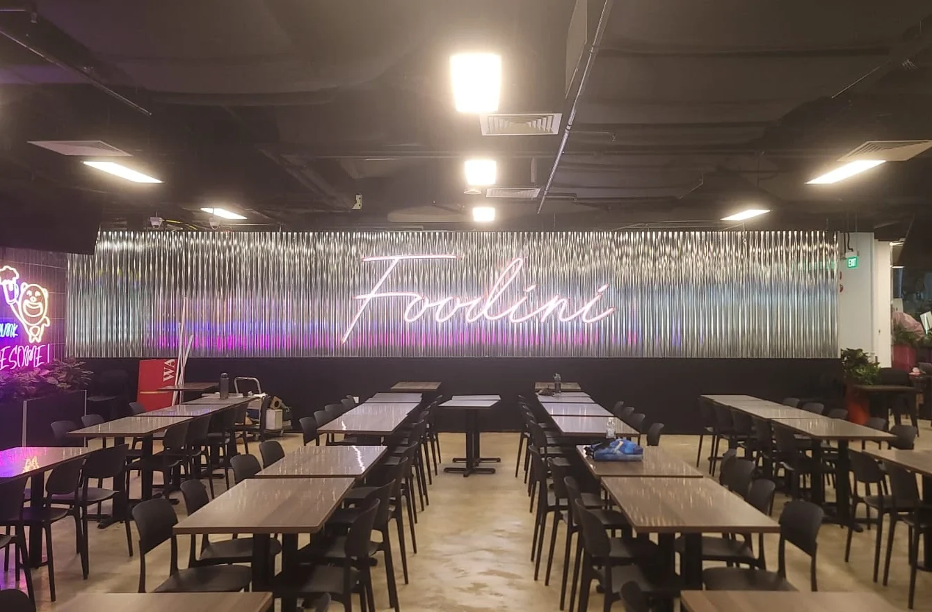 A glowing pink neon sign spelling "Foodini" is mounted on a corrugated metal accent wall in the background
