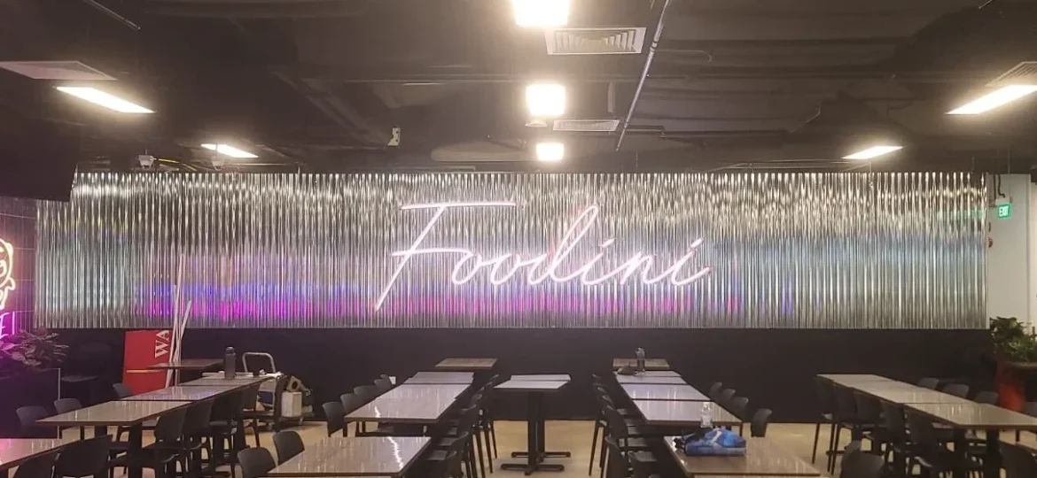 A glowing pink neon sign spelling "Foodini" is mounted on a corrugated metal accent wall in the background