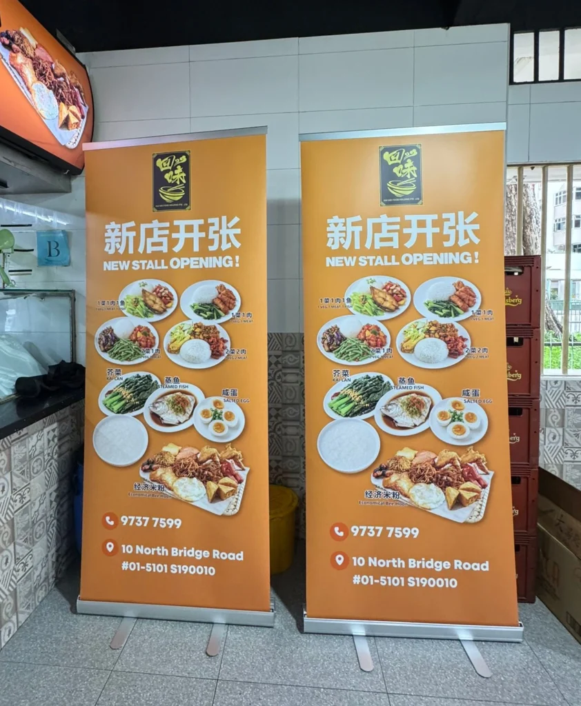 Two pull-up banners with food photos and contact details inside a food court area.