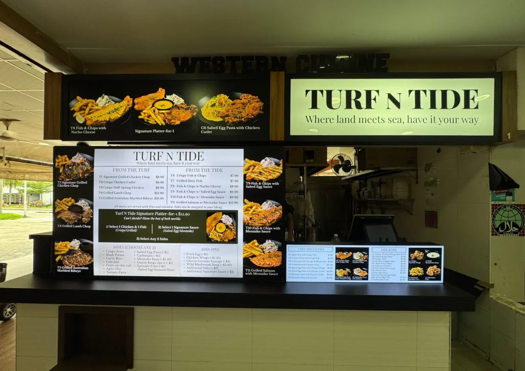 An illuminated food stall counter displaying glowing menu boards with photos and prices