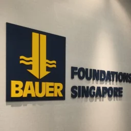 Black and yellow 3D acrylic logo letters mounted on a grey textured office wall