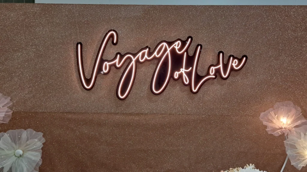 A warm LED neon signage mounted on a shimmering bronze backdrop framed with decorative flowers.