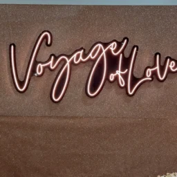 A warm LED neon signage mounted on a shimmering bronze backdrop framed with decorative flowers.