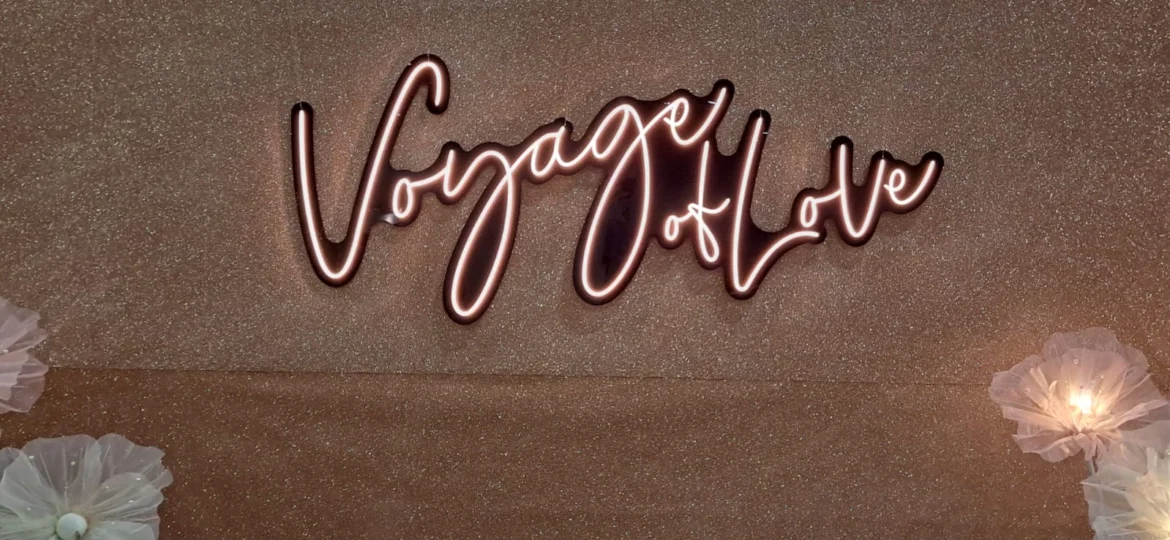 A warm LED neon signage mounted on a shimmering bronze backdrop framed with decorative flowers.